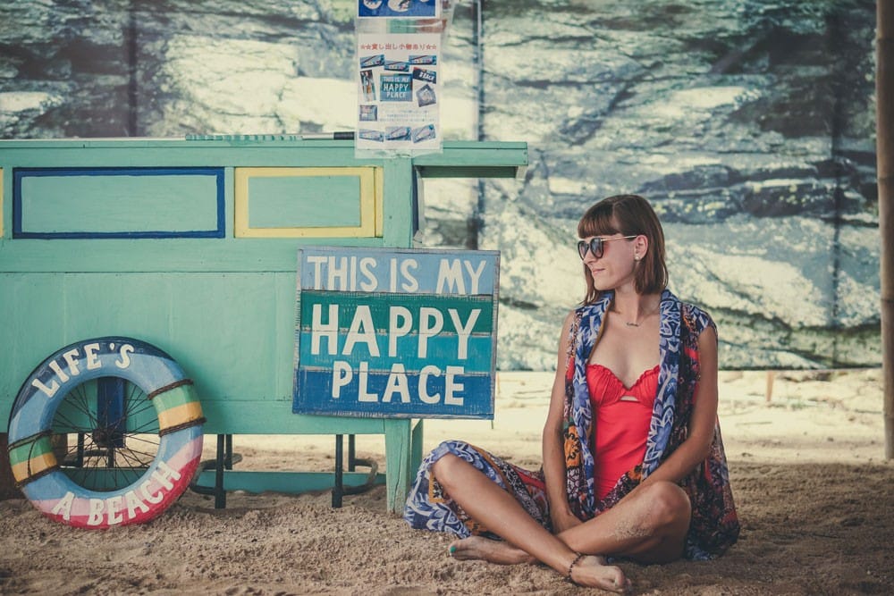 Viajar por el mundo chica morena con un bañador roja sentada y al lado un cartel inspirador